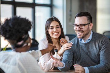 Close up photo of broker giving keys of new house to happy couple. Young happy couple smiling and getting keys from new real estate from agent. Real estate agent handing over the key