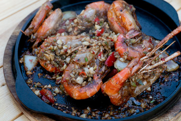 Close up of Prawn river with fried garlic in hot pan. Ready to be served on a wooden table.