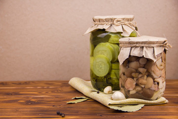 fermented pickled canned zucchini and mushrooms in jars  garlic bay leaf black pepper peas on a piece of burlap on brown wooden background