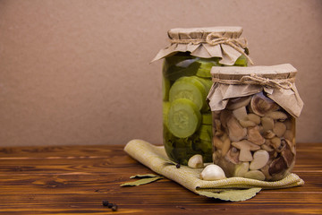 fermented pickled canned zucchini and mushrooms in jars  garlic bay leaf black pepper peas on a piece of burlap on brown wooden background