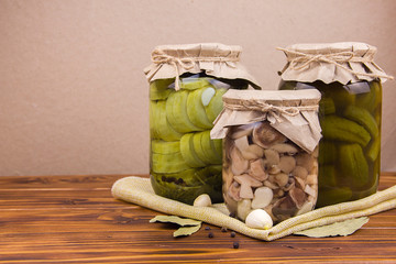fermented pickled canned zucchini and cucumber mushrooms in jars garlic bay leaf black pepper peas on a piece of burlap on a brown wooden background