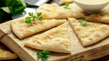 Fresh slices of Garlic pizza on wooden board with herbs.