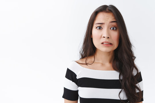 Embarrassed and confused insecure young asian female made mistake, feel sorry or pity, cringe nervously, clench teeth and pulling sad worried face, frowning panicking, standing white background