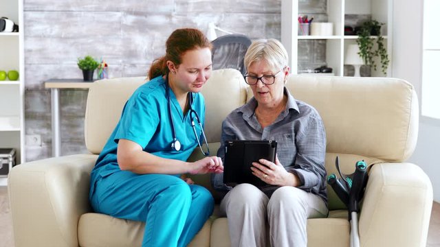 Female nuse helping senior elderly retired woman how to use her tablet computer
