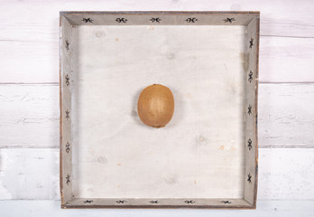 A kiwi placed in the middle in an old wooden tray on a background of old wooden floor