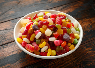 A mix of colorful candy in white bowl on wooden table
