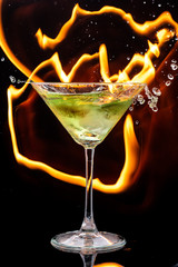 ice falls on a martini glass on a black background and lines of fire in the dark