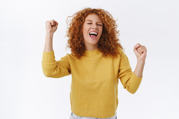 Joyful, redhead curly woman celebrating win, feeling lucky and relieved, yelling yes, achieve...