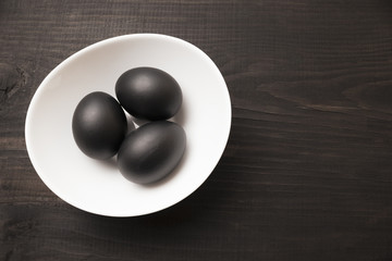 Eggs painted black lie in a white plate. Eggs in a bowl on a black wooden background. Preparing for Easter. Cooking food.