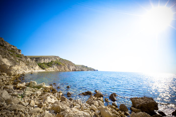Seascape of still blue sea waters shore, stone beach and green rock