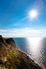 Seascape of still blue sea waters shore, rocky coastline and bright sun