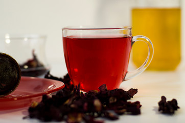 A Cup of red tea on a white table. Hibiscus brewed in a transparent Cup. Dried hibiscus brewed with boiling water.