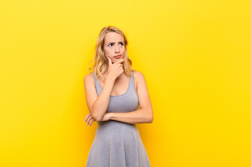 young blonde woman thinking, feeling doubtful and confused, with different options, wondering which...