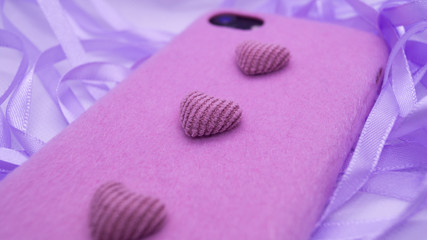 Phone in a pink soft case with hearts on a lilac satin ribbon. Focus on the heart in the middle.