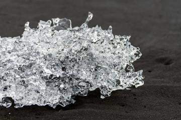 Crystal clear ice chunks washed up on the black lava sand by the waves on diamond beach in Jokulsarlon glacier lagoon. Climate change and glacier melting concept.