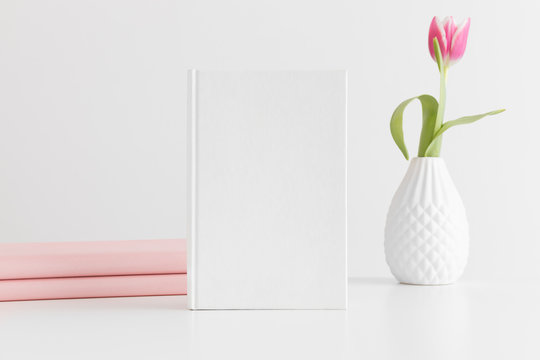 White book mockup with a pink tulip and books on a white table.
