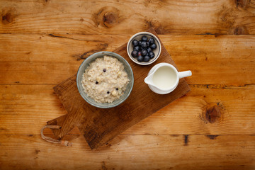 Blueberry and apple porridge and a small bowl of blueberries and a jug of milk, on a wooden board, on a wooden backdrop