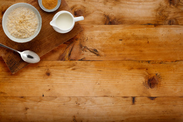 A nutritious bowl of porridge, a small bowl of brown sugar and a jug of milk with a spoon, on a wooden board, on a wooden background with space for copy