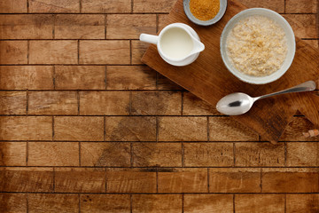 A nutritious bowl of porridge, a small bowl of brown sugar and a jug of milk with a spoon, on a wooden board, on a checked wooden background with space for copy