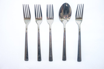 A spoon amongst a row of forks.