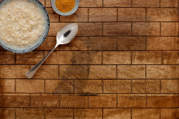 A nutritious bowl of porridge, a small bowl of brown sugar with a sppon, on a checked wooden background with spaace for copy