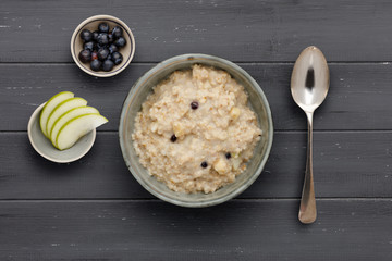 A bowl of nutritious blueberry and apple porridge and a small bowl of  apple and blueberries, with a spoon, on a dark wooden background