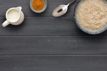 A nutritious bowl of porridge, a small bowl of brown sugar, a jug of milk and a spoon, on a dark wooden background, with rcopy space