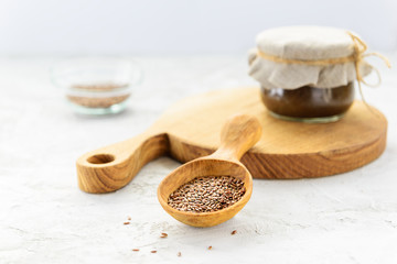 Flaxseeds in a wooden spoon with linseed in a jar on a gray table.