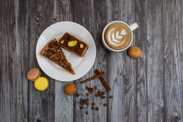 Cup of coffee and two slices of cake and macaroons on the plate on wooden table