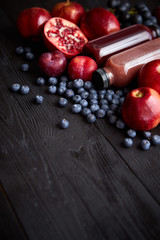 Various fresh red, purple black fruits. Mix of fruits and bottled juices on black