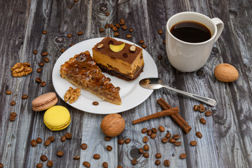 Cup of coffee and two slices of cake and macaroons on the plate on wooden table
