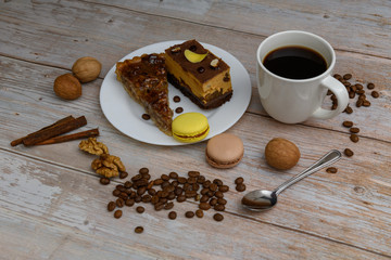 Cup of coffee and two slices of cake and macaroons on the plate on wooden table