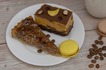 Cup of coffee and two slices of cake and macaroons on the plate on wooden table
