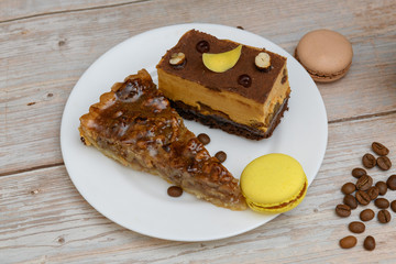 Cup of coffee and two slices of cake and macaroons on the plate on wooden table
