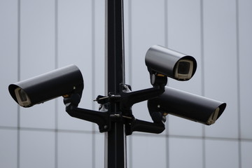 Video surveillance system on a pole, three cameras are turned in different directions to cover the visibility of the entire territory. CCTV camera operating watching city security in the background