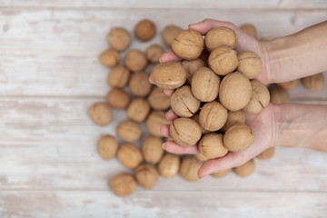 Hands holding whole walnuts on rustic old wooden table