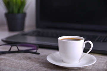 Cup of coffee on office desktop with laptop, computer on wooden table. Close up, with space for your text