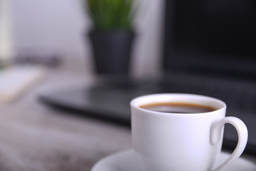 Cup of coffee on office desktop with laptop, computer on wooden table. Close up, with space for your text