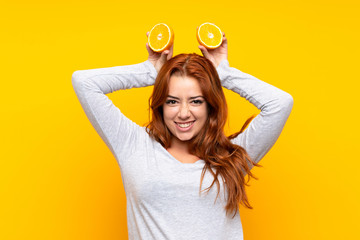 Fototapeta na wymiar Teenager redhead girl holding an orange over isolated yellow background