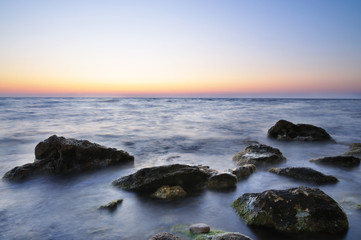 Fototapeta na wymiar Beautiful pink sunset over still sea waters and water stones with green moss in Crimea