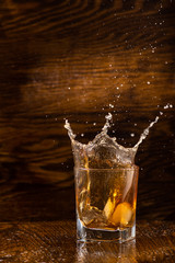 big splash in a glass with whiskey with ice on a dark wooden background