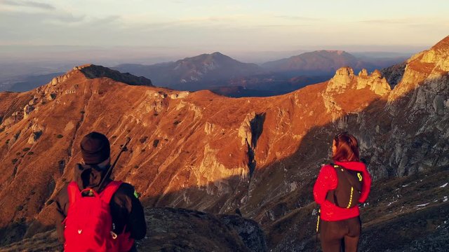 Aerial 4k drone clip with couple of hikers watching a beautiful sunset on top of Bucegi mountain ridge, during magical golden hour light in autumn season, in Romania