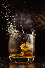 big splash in a glass with whiskey with ice on a dark wooden background