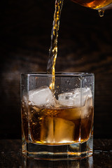 pour whiskey in a glass with ice on a dark wooden background close-up