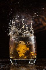 big splash in a glass with whiskey with ice on a dark wooden background