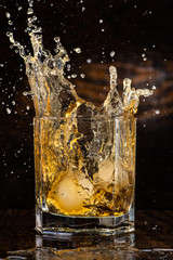 big splash in a glass with whiskey with ice on a dark wooden background