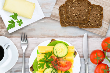 Top view of healthy and energetic breakfast - coffee, butter, dark bread, tomatoes and vegetable sandwich with cheese on a wooden vintage table.
