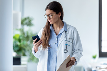 Pretty female doctor using her mobile phone while standing in medical consultation.