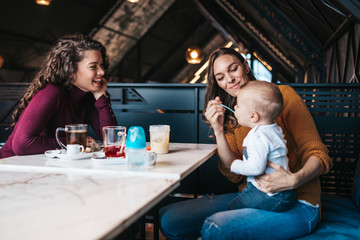 Two friends enjoying in cafe bar with cute little baby boy.