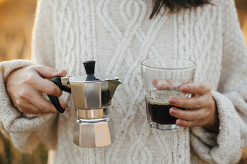 Fototapeta na wymiar Alternative coffee brewing in travel. Hipster woman holding geyser coffee maker and glass cup with coffee in sunny warm light in rural countryside herbs. Atmospheric moment.